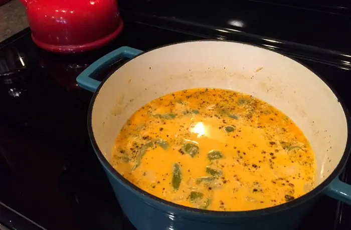 A close-up shot of the best Thai Coconut Chicken Soup in a blue enamel coated pot on a stovetop.