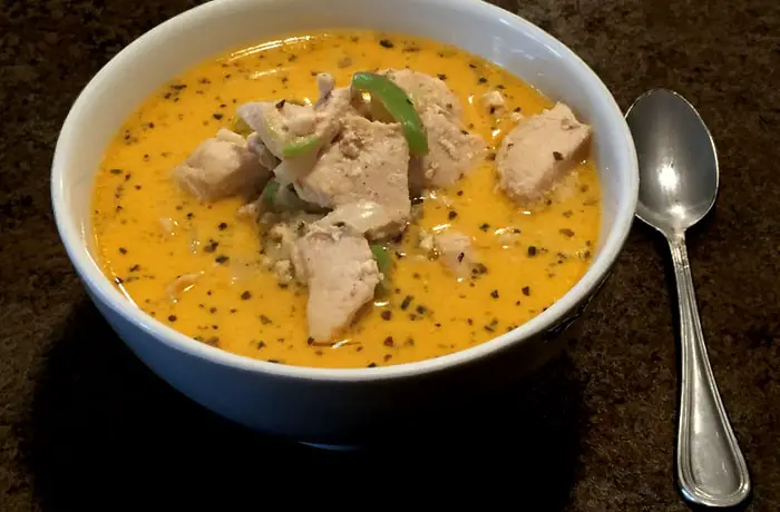 A close-up shot of the best Thai Coconut Chicken Soup in a white a bowl with a brown countertop background
