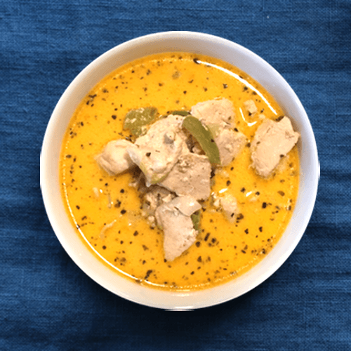 A close-up shot of the best Thai Coconut Chicken Soup in a white a bowl with a blue tablecloth background