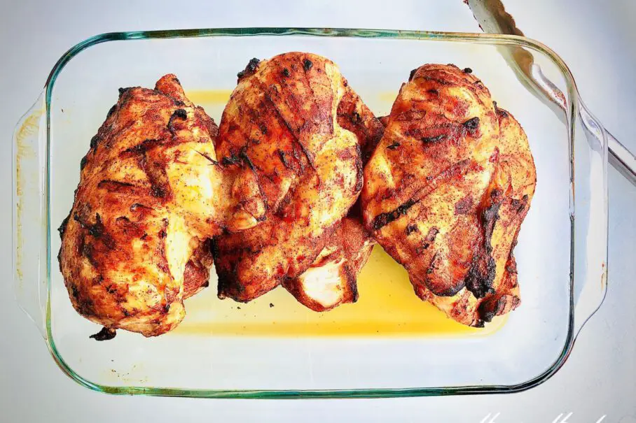 Three grilled chicken breasts in a glass baking dish with a fork and a watermark on a white background
