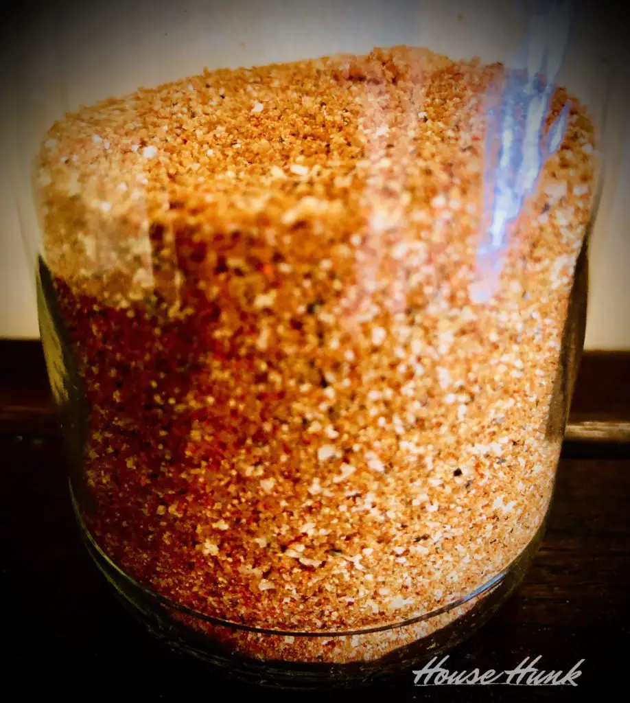 A glass jar filled with a brown sugar mixture on a wooden surface. The mixture looks like it has spices in it. The text “House Hunk” is in the bottom right corner of the image.