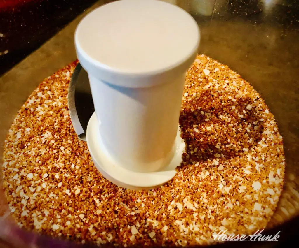 Spices and brown sugar in a food processor bowl ready to be blended. The spices are paprika, salt, and black pepper. The bowl is clear plastic and has a metal blade in the center.