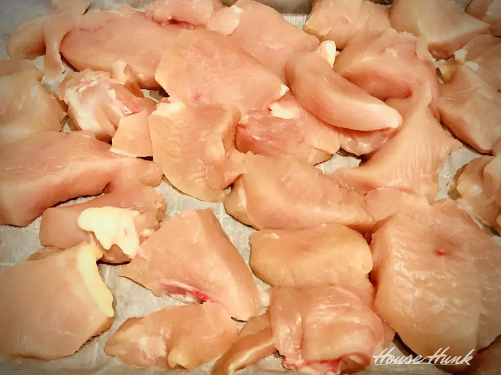 cut up frozen chicken breasts on a parchment lined tray