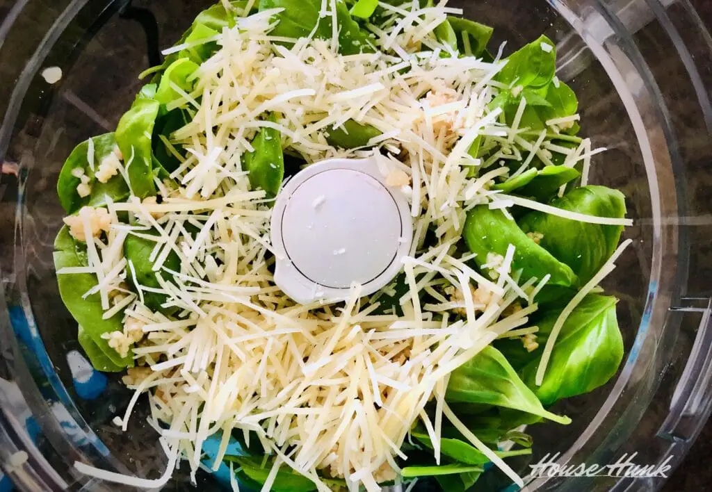 An overhead photo of nut-free pesto recipe ingredients being prepared in a food processor.