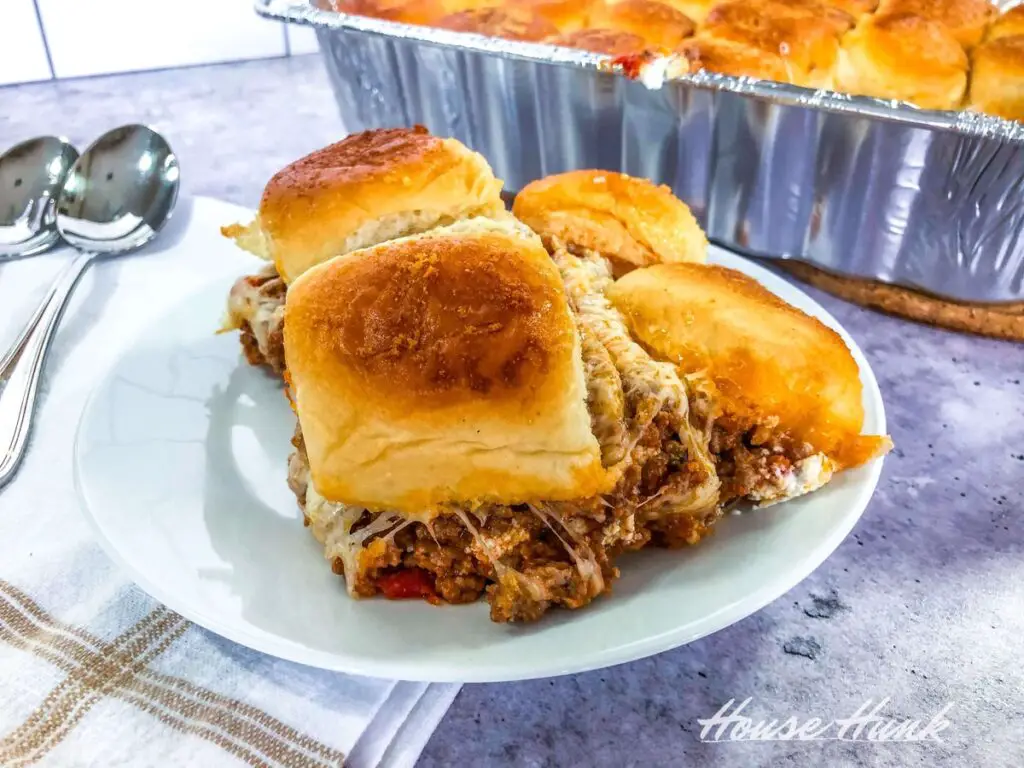 A closeup shot of four of the best Lasagna Sliders on a white plate with an aluminum lasagna pan in the background.