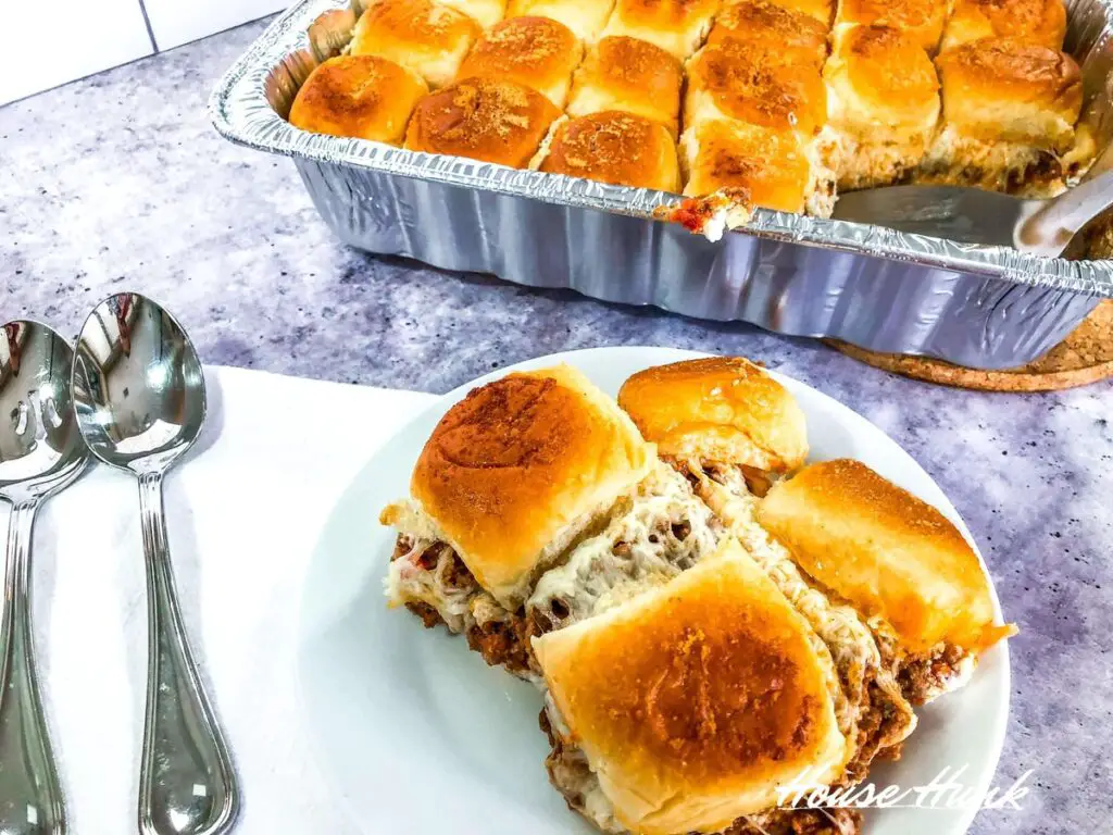 Four of the best lasagna sliders on a white plate being served from an aluminum lasagna pan with a metal spatula.
