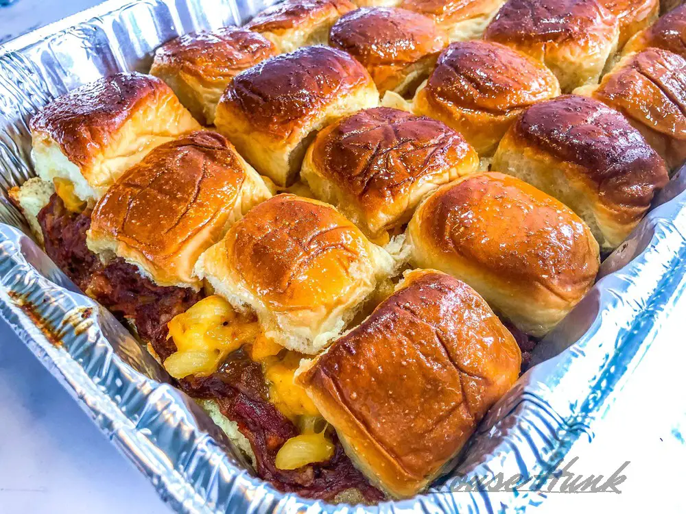 An aluminum baking tray of the best macaroni and cheese topped pulled pork sliders on a marble countertop