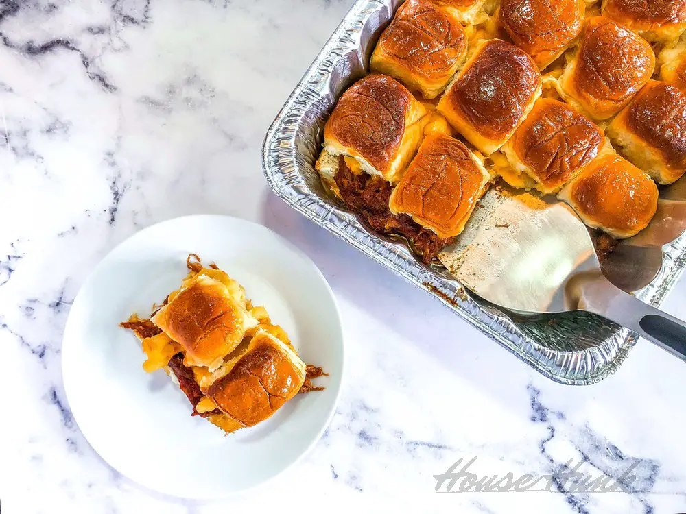 An overhead image of a tray of the best macaroni and cheese topped pulled pork sliders on a marble countertop