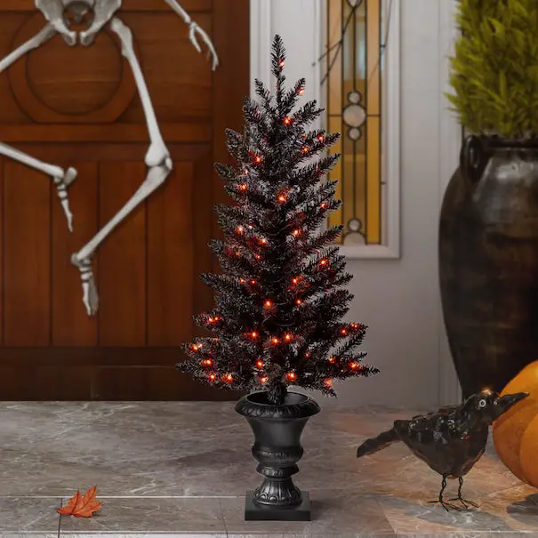 A spooky black Christmas tree with orange lights and a bird figurine on a marble surface with a wooden door and a vase in the background