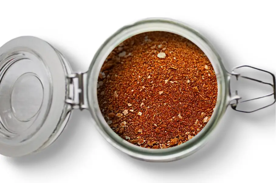 A photo of an open jar of homemade Spanish rice seasoning on a white background.