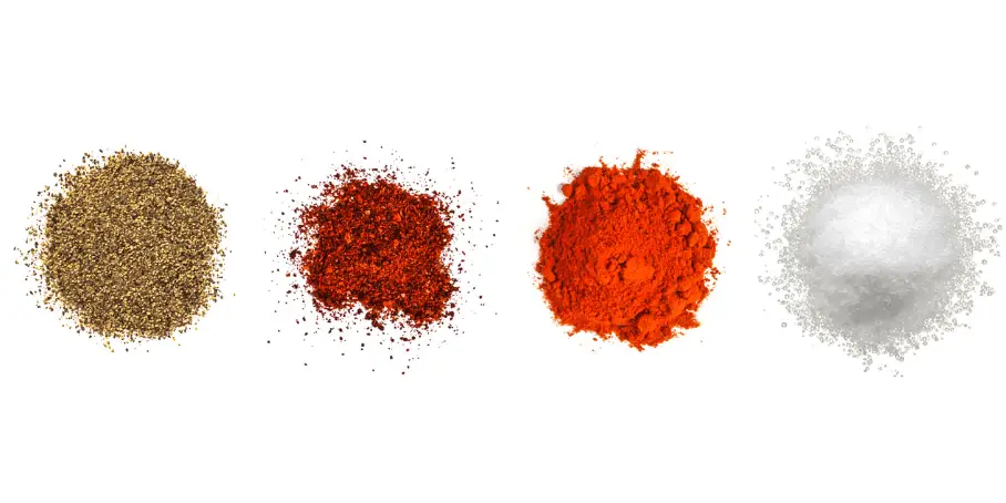 A photorealistic image of ingredients for Homemade Crab and Shrimp Boil Spice Blend consisting of four piles of different spices and herbs on a white background.