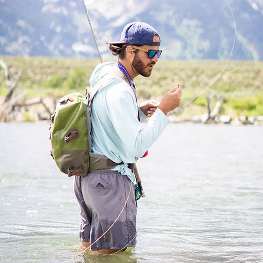 A man fly fishing in a river wearing the Give'r Solstice Solar Hoodie in Beach Blue