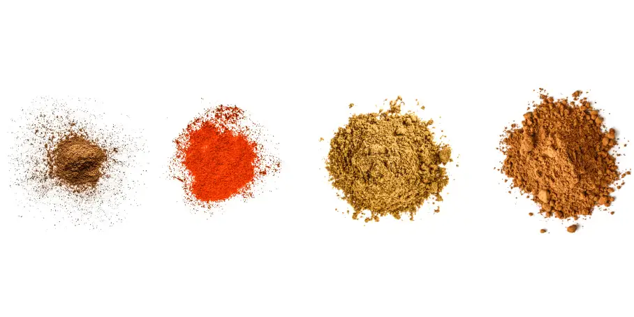 A photorealistic image of ingredients for Homemade Dry Mexican Mole Spice Blend consisting of four piles of different spices and herbs on a white background.