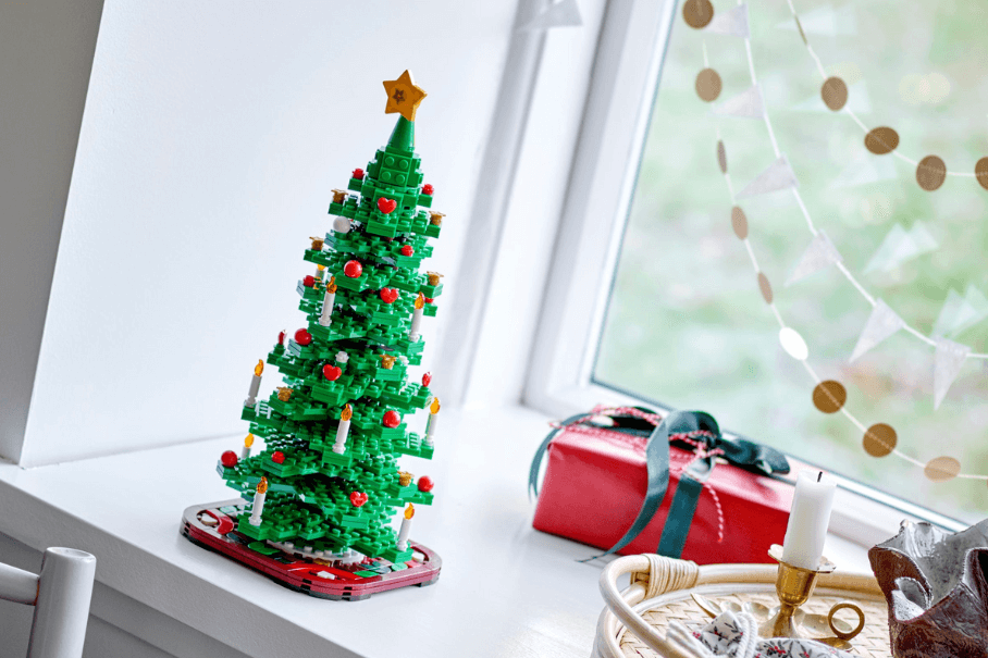 A festive LEGO Christmas Tree sits on a window sill beside a wrapped present with a red paper and green ribbon.