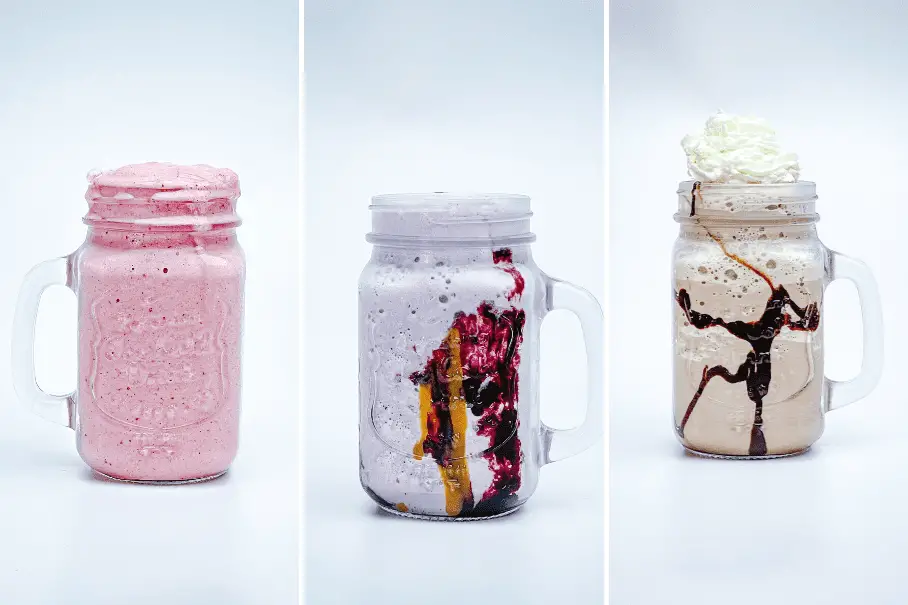 Three different smoothies in mason jar mugs on a white background. The first smoothie is pink. The second smoothie is white with a purple swirl. The third smoothie is beige with a chocolate drizzle and whipped cream.