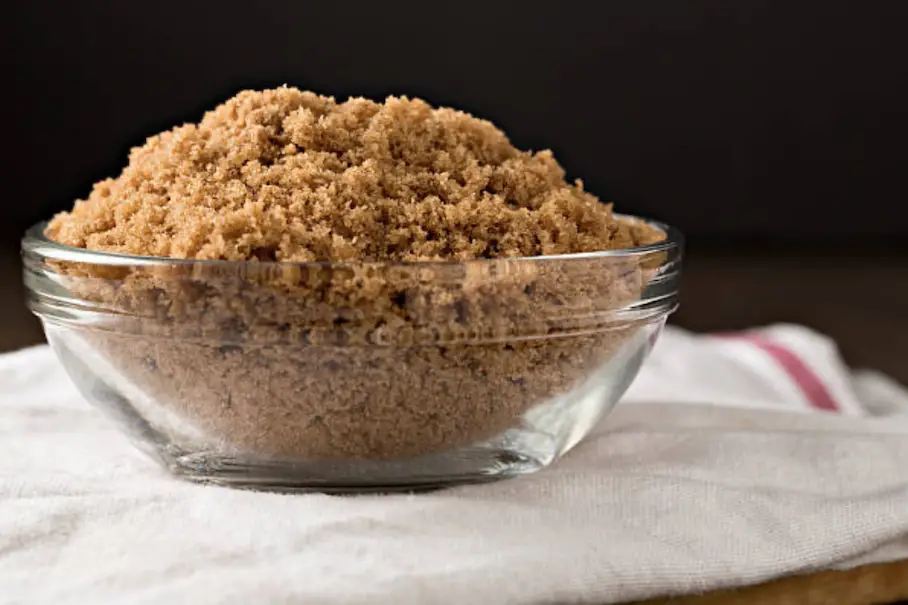 A glass bowl of brown sugar on a cloth towel.