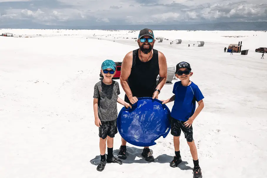 A father and two boys joyfully sledding down a sand dune at White Sands National Park