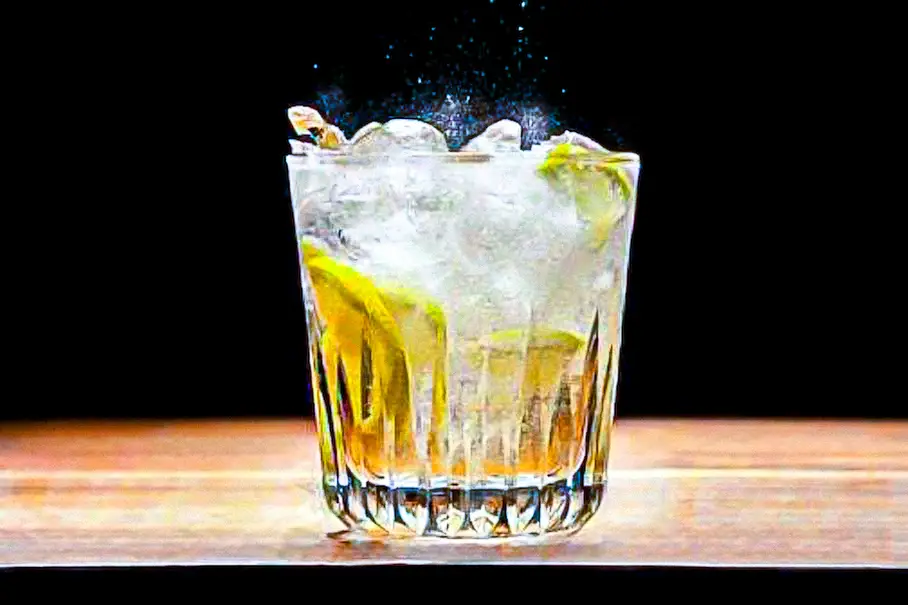 A clear glass of vodka and bitter lemon with carbonation, set against a black background on a wooden table