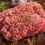 A photo realistic image of a spiced raw ground veal on a wooden cutting board with a sprig of parsley.
