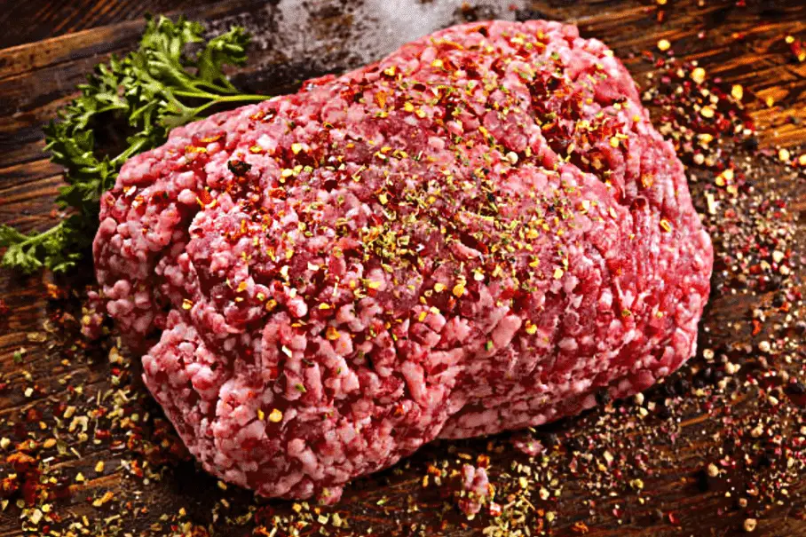 A photo realistic image of a spiced raw ground veal on a wooden cutting board with a sprig of parsley.