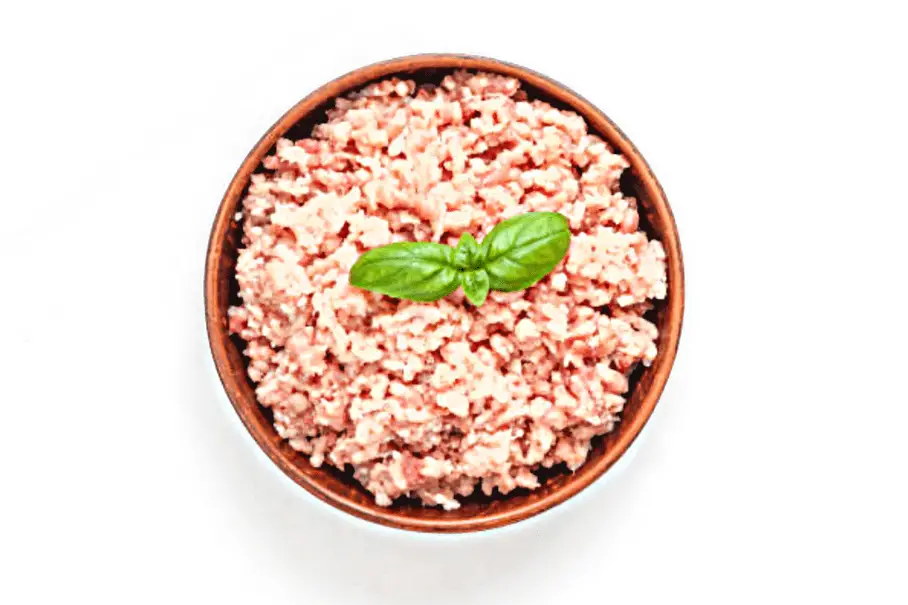 A photo realistic image of a bowl of ground turkey meat with a basil leaf on a white background.