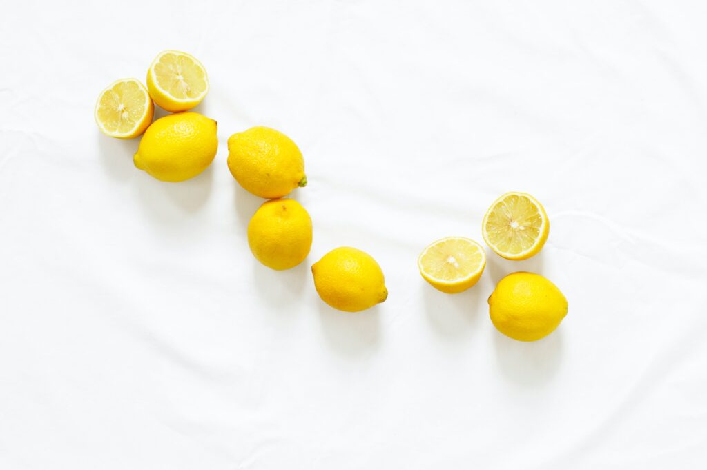 A pile of fresh lemons, some whole and some cut in half, on a white background.