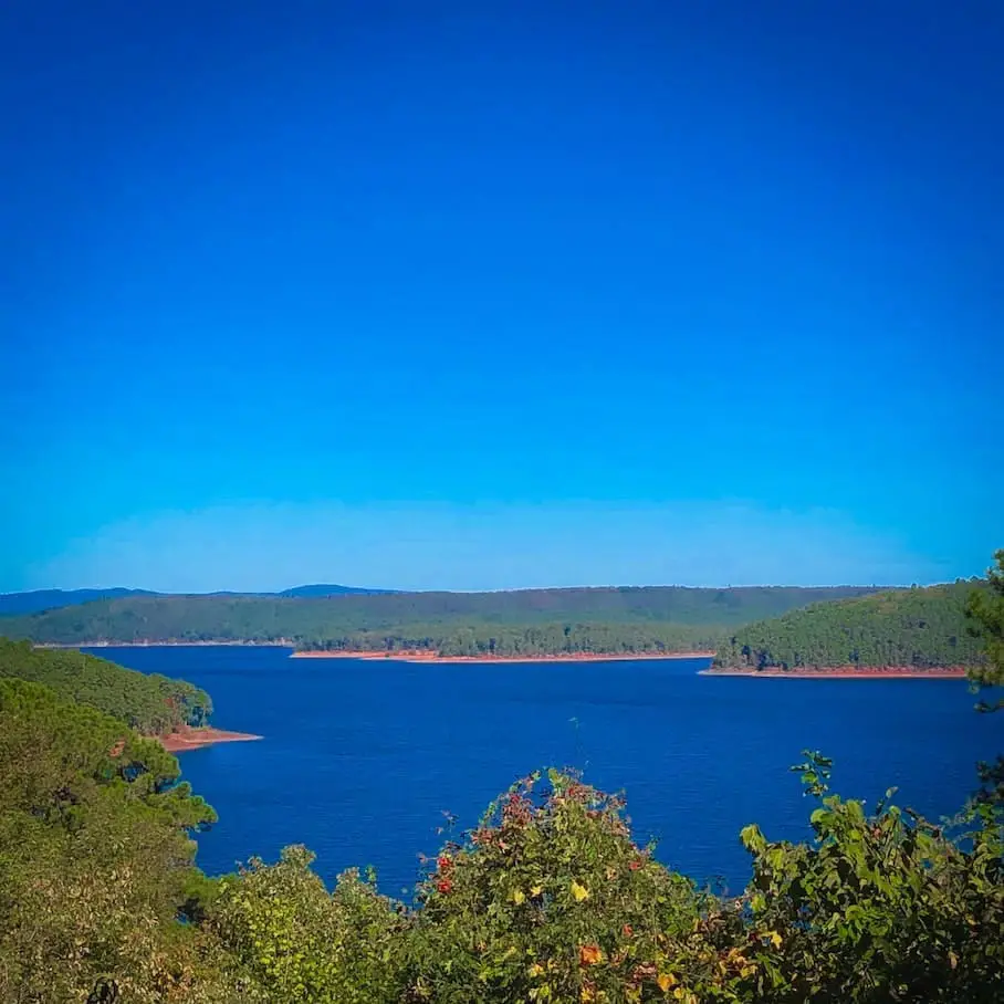 A picturesque view of Lake Greeson in Arkansas with a bright blue sky and dark blue water in the distance.