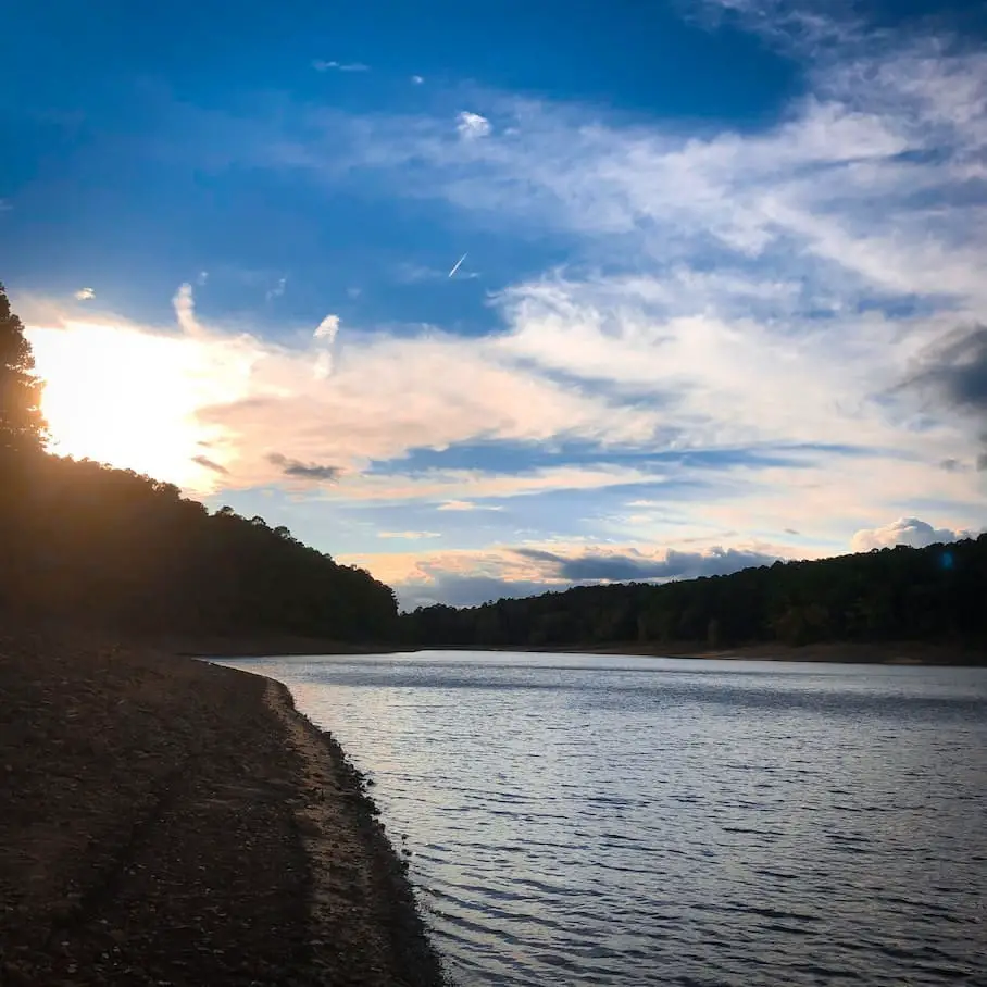 A sunset view from the shore of Lake Greeson with a partially cloudy sky