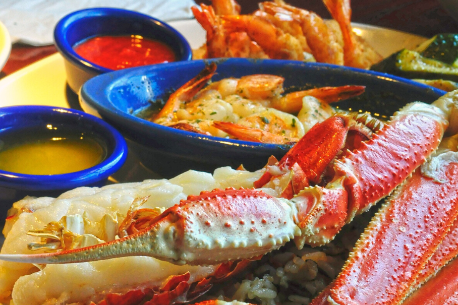 A photo of a seafood platter with lobster, shrimp, and crab legs with three sauces on a wooden table.