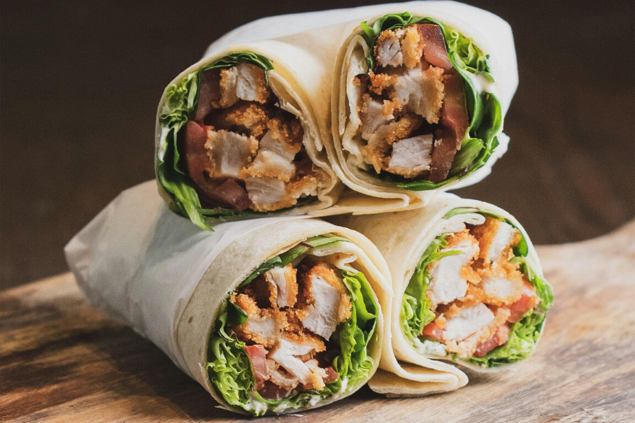 A photo of three chicken shawarma wraps with lettuce and sauce on a wooden surface.
