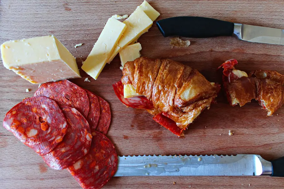 A charcuterie board with meats, cheeses, and a croissant on a wooden surface.