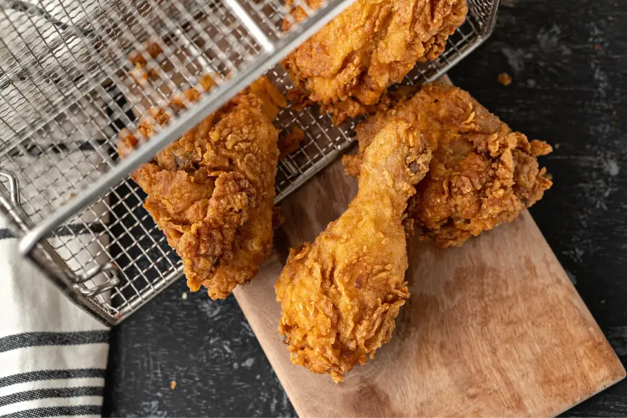 Fried chicken in a wire frying basket on a wooden cutting board on a black countertop.