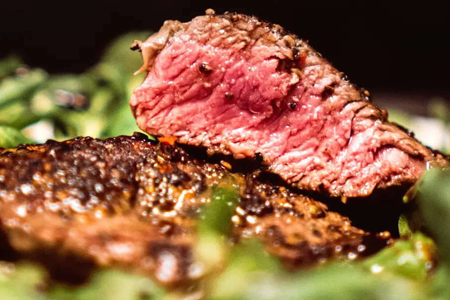 A close-up of a sliced medium rare steak on greens with a charred crust.