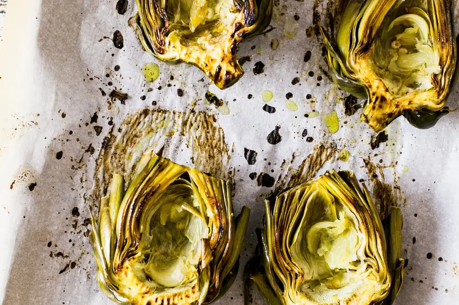 Roasted artichokes with pepper and herbs on a baking sheet with parchment paper.