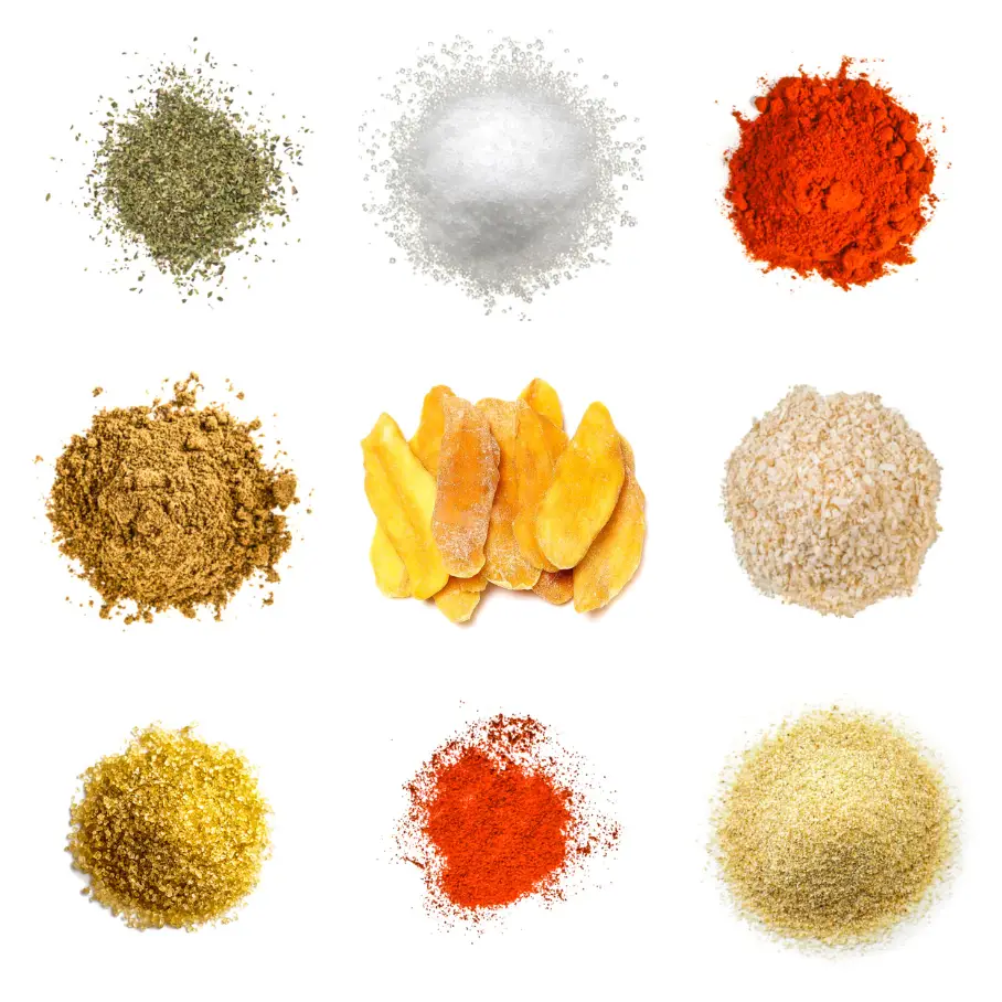 A grid of nine spices and seasonings on a white background, including oregano, salt, paprika, cumin, dried mango, sesame seeds, turmeric, chili powder, and garlic powder.