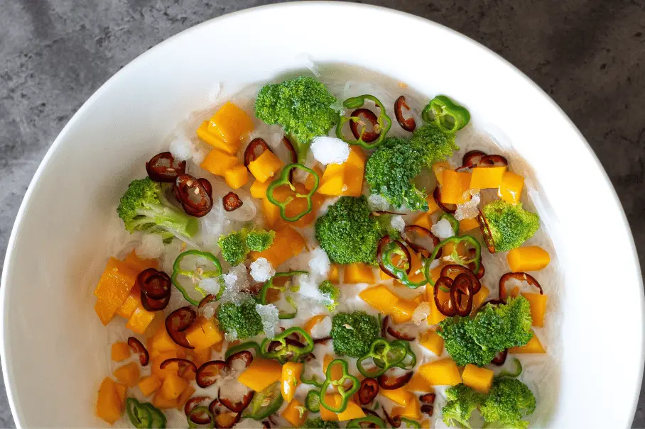 A bowl of vegetable dish with broccoli, butternut squash, and red chili peppers.