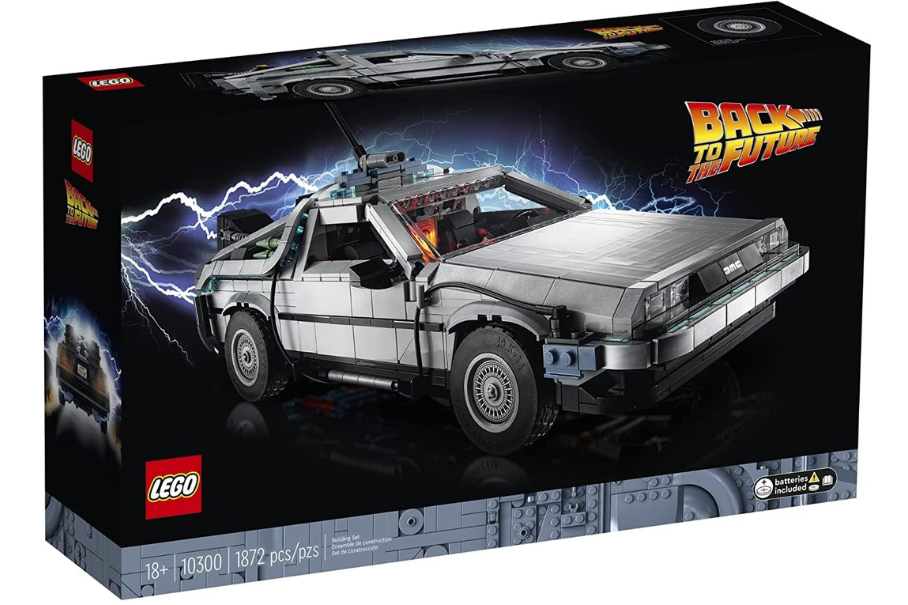 A LEGO set box for the “Back to the Future” DeLorean car is shown on a black background. The box has a picture of the silver car with a red stripe and a red “OUTATIME” license plate. The car has a flux capacitor and other time travel equipment on the roof. The box has the LEGO logo and the “Back to the Future” logo on it. The box also has the age recommendation (18+) and the number of pieces (1872) on it.