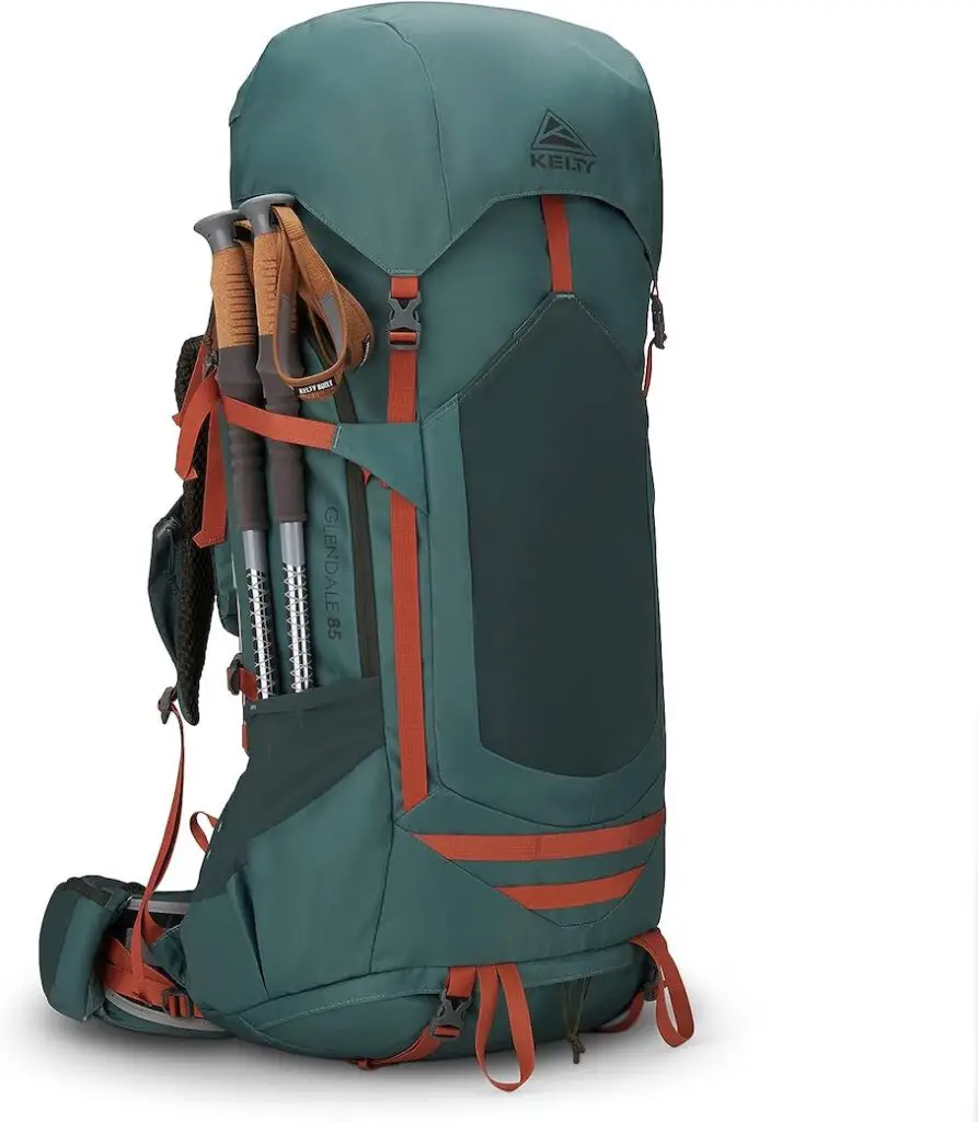 A green hiking backpack with orange accents on a tree bark. The backpack has a large main compartment, two side pockets, a padded back panel, shoulder straps, a waist strap, a trekking pole attachment, and a “KELTY” logo.