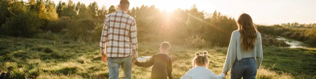 a family holding hands walking through a field during sunset